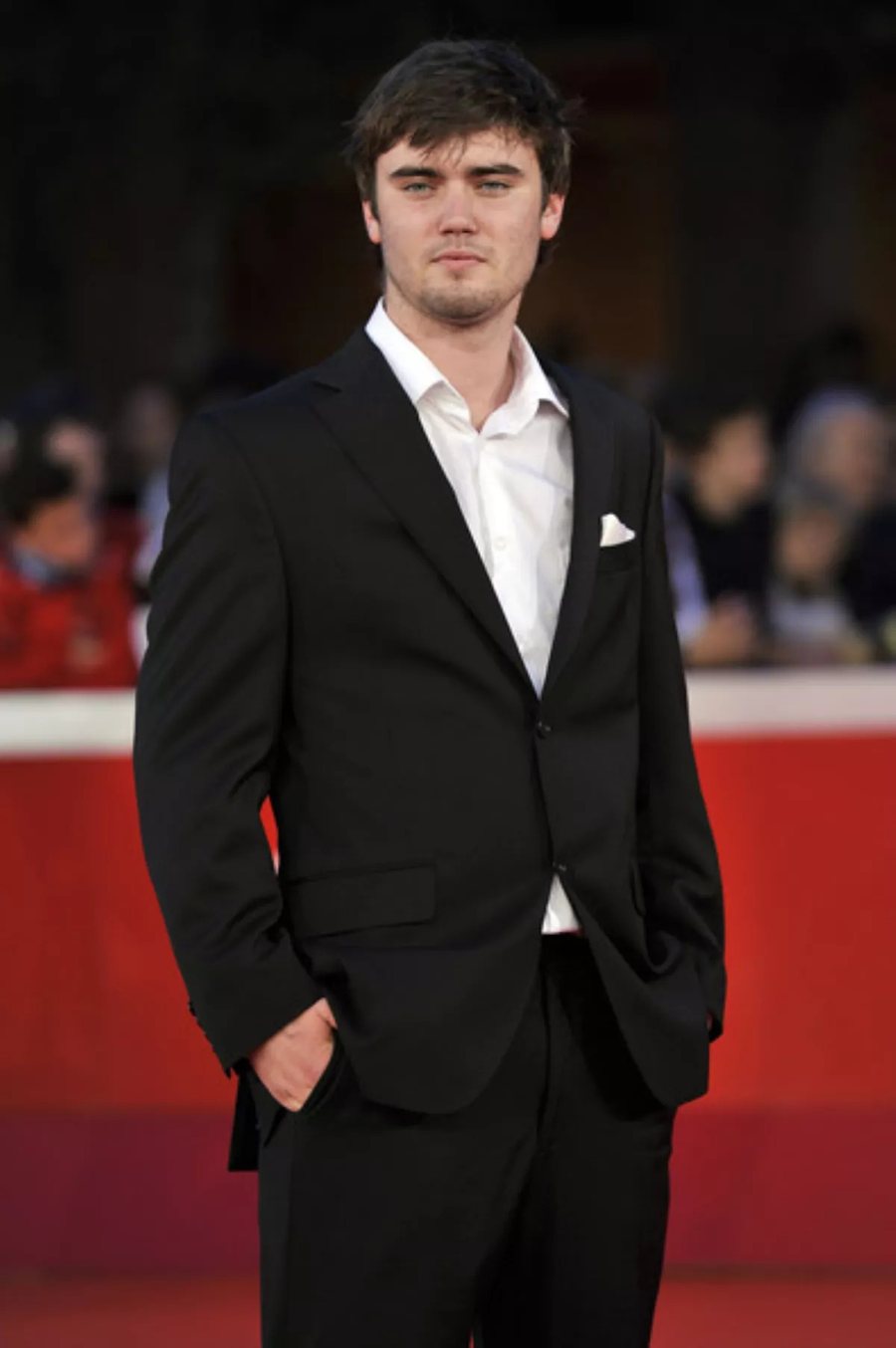 Cameron Bright in a dark suit and white shirt on a red carpet